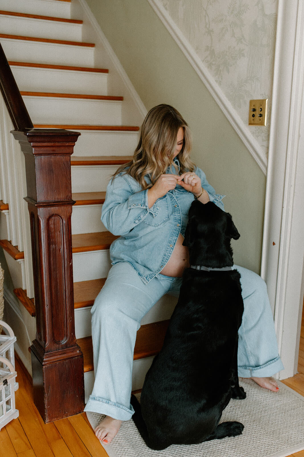 Expecting mother sitting on the stairs and cuddling with her black dog.
