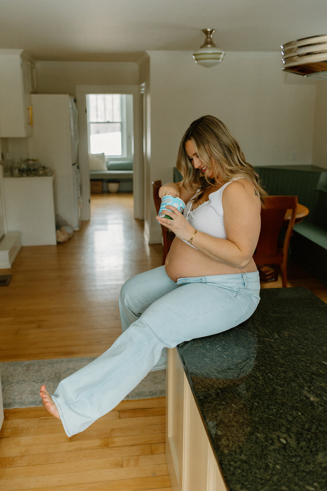 Candid of an expectant mother sitting on the kitchen counter and eating a snack.