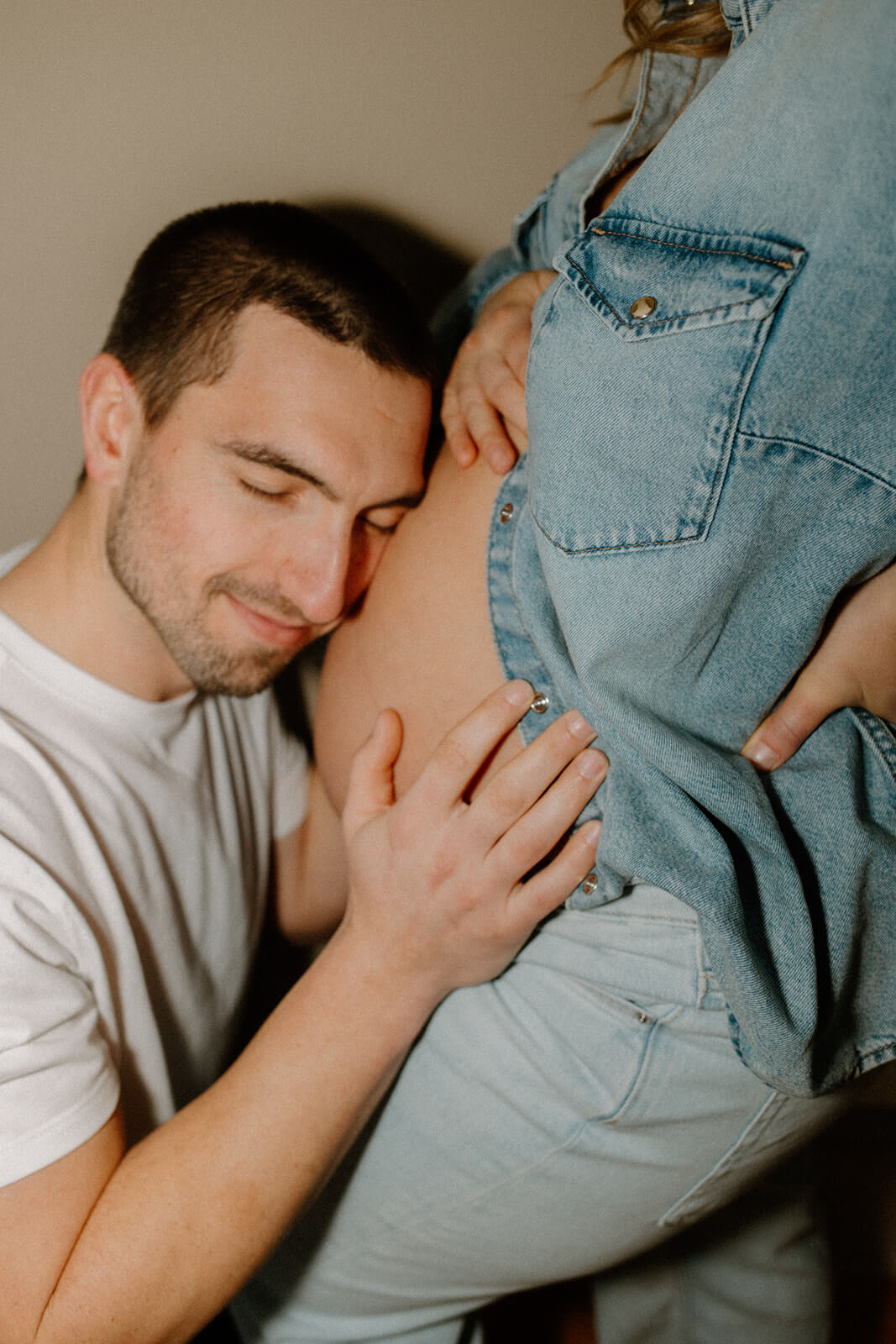 Close-up of expecting father resting his head and hand against his partner’s baby bump.