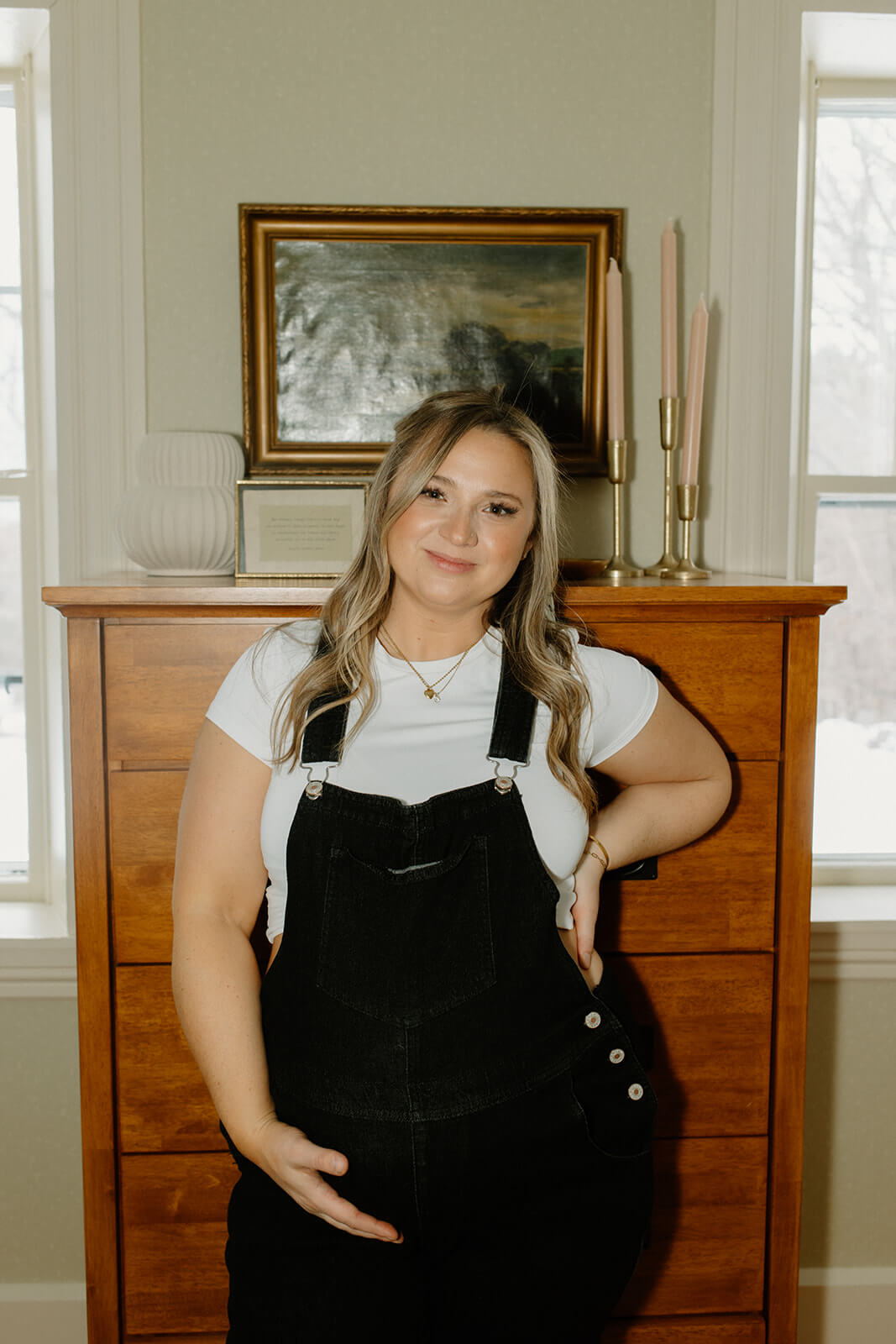 portrait of an expecting mother wearing black overalls and holding her baby bump.