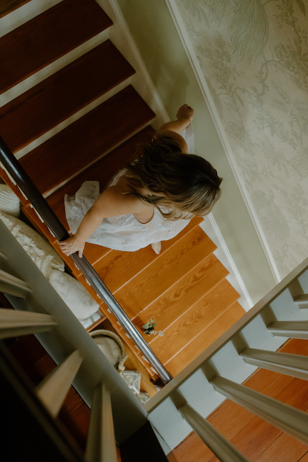 Overhead maternity photoshoot at home of an expecting mother in a flowing maternity dress walking down the staircase.