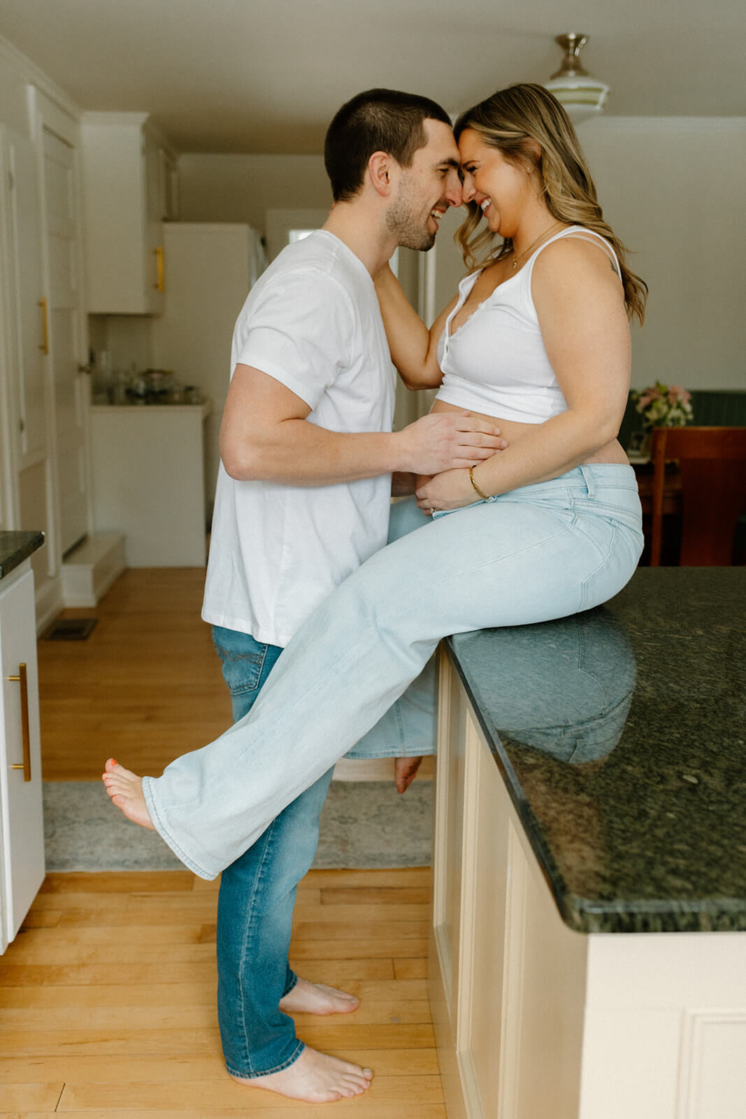 Maternity photoshoot at home with an expecting couple smiling forehead to forehead while she sits on the kitchen counter.