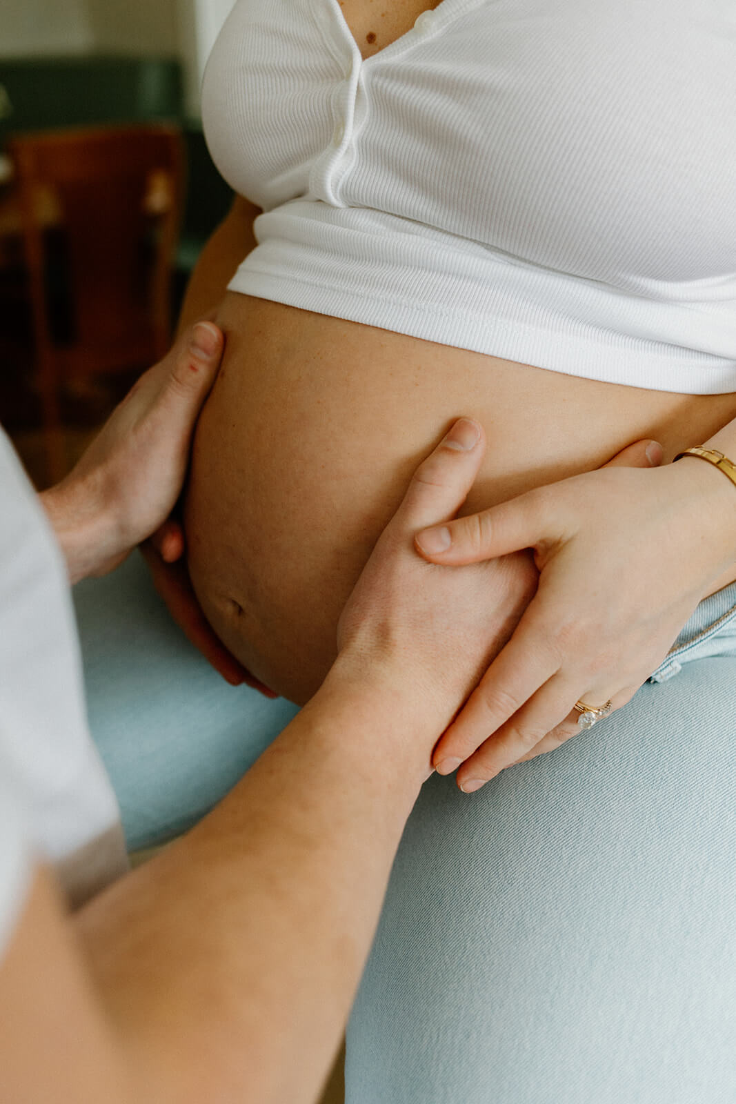 Close-up of an expecting mother’s belly with her partner’s hands resting gently around it.